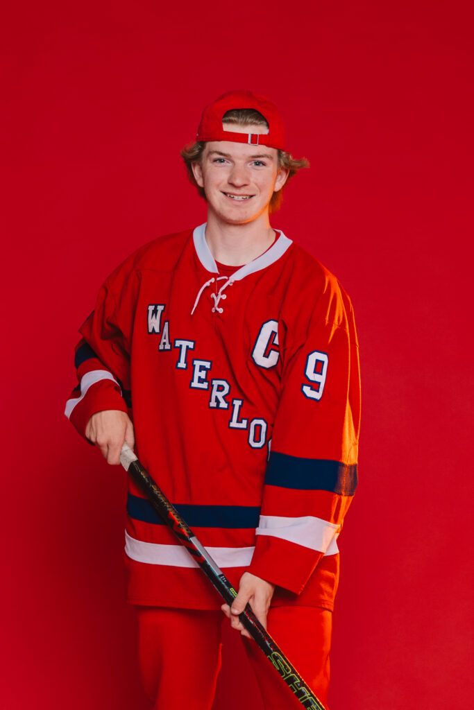 Kansas City senior boy posing in photography studio with hockey stick and gear for sports senior portraits