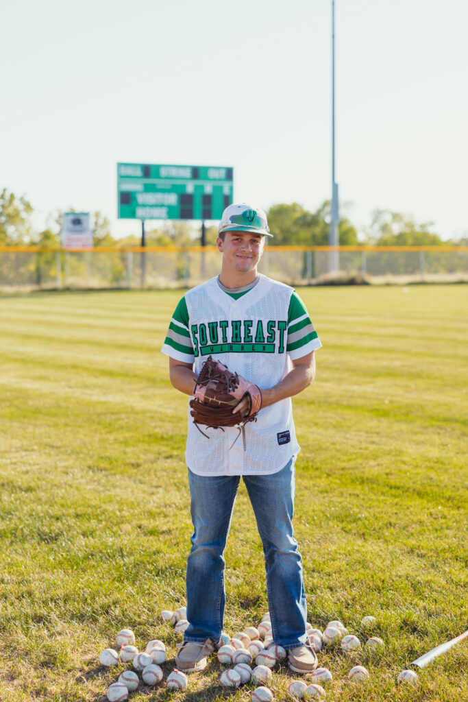 Kansas City senior baseball player posing on field with glove and baseballs during senior session