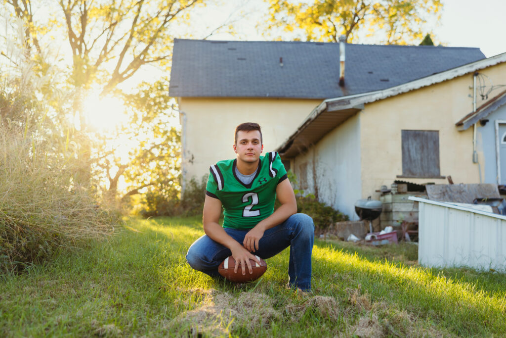 Kansas City senior boy outdoors in football jersey holding football during senior session