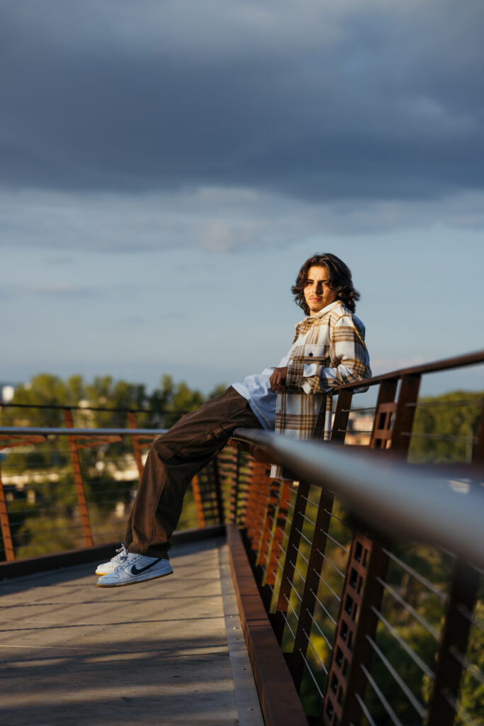 High school senior boy sitting on railing at golden hour