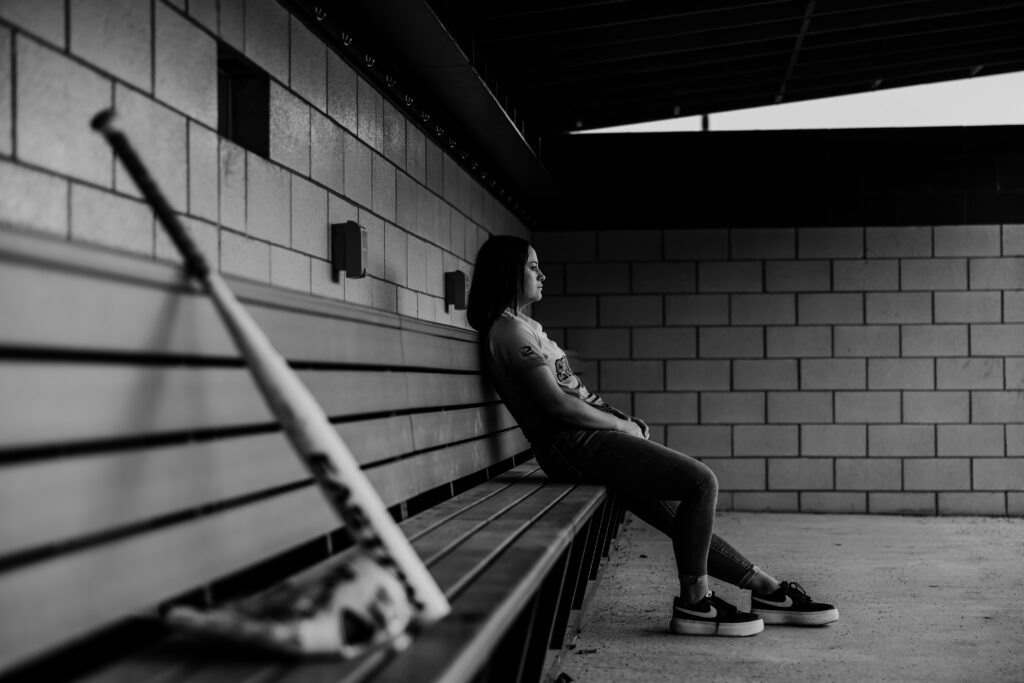 Kansas City senior girl posing in softball dugout during sports portraits