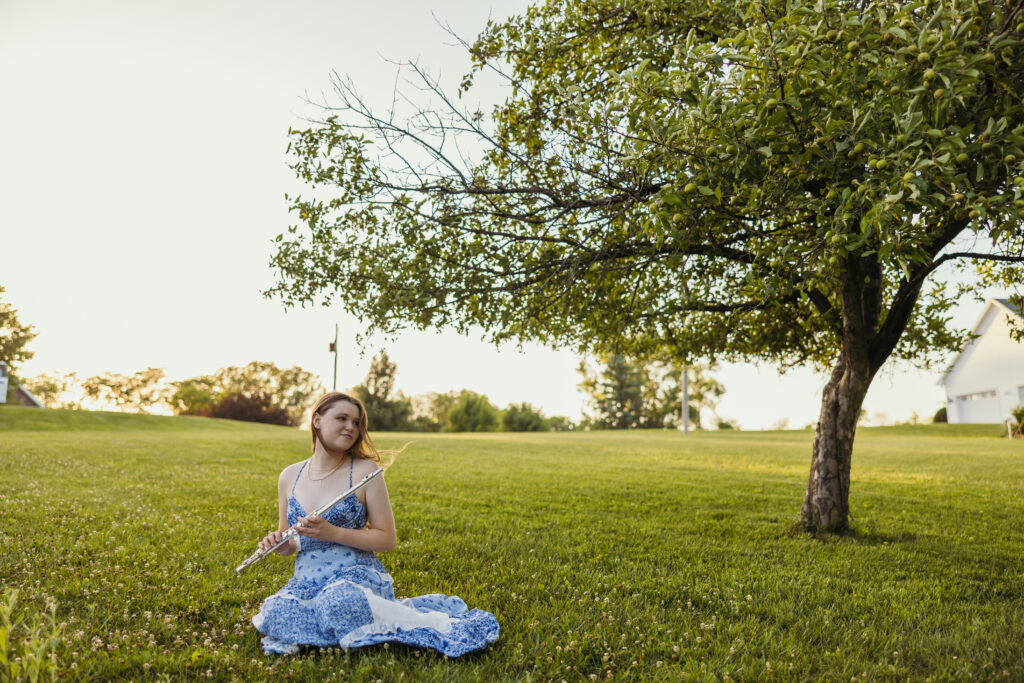 Senior girl musician holding flute in grassy field with wildflowers for outdoor senior photos