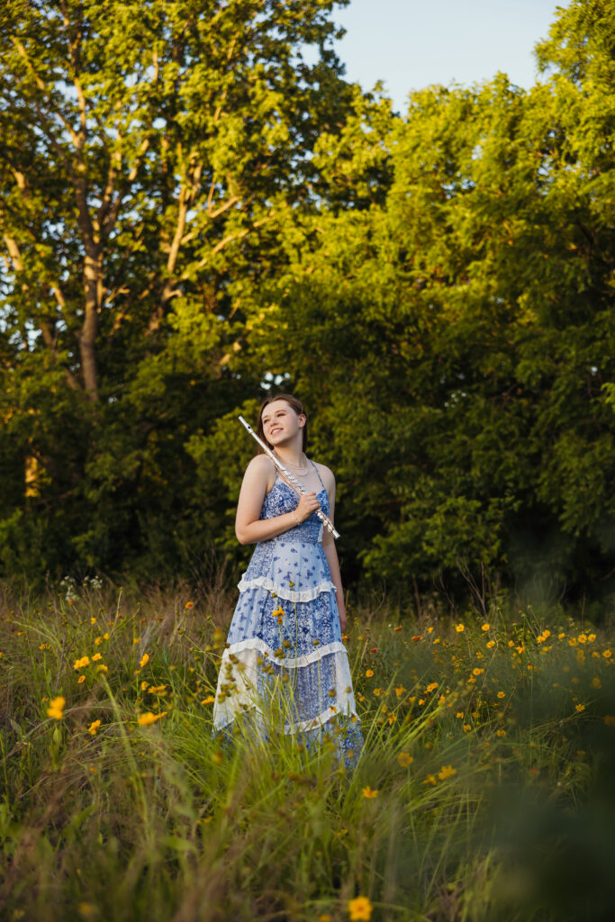 High school senior girl posing with flute in open field with wildflowers during Kansas City senior session
