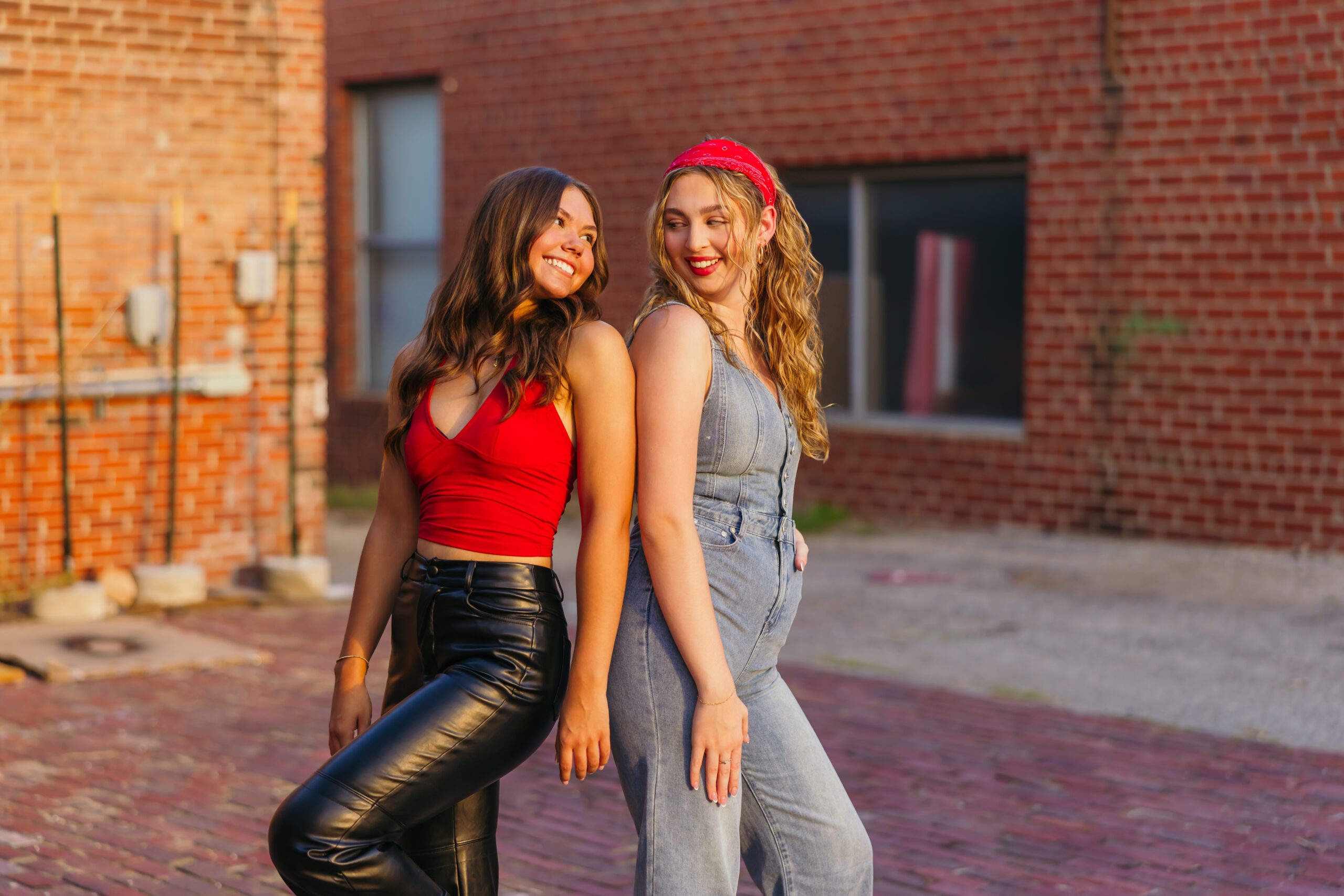 Two high school senior girls with red accent clothing during senior photo session with brick buildings