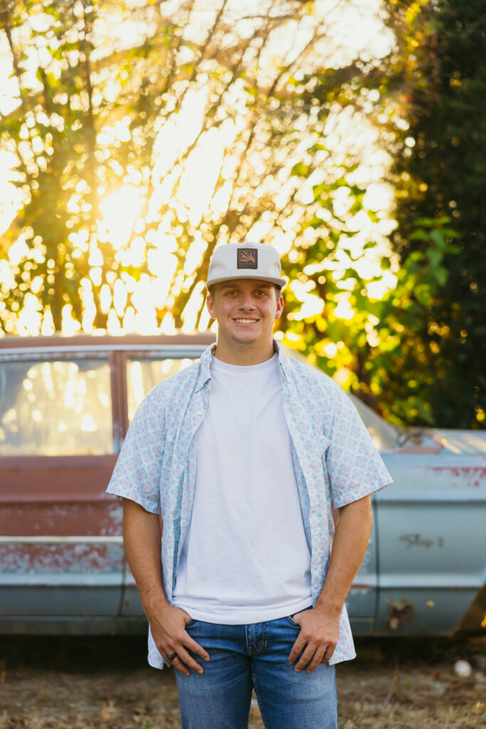 High school senior boy with old car wearing baseball hat