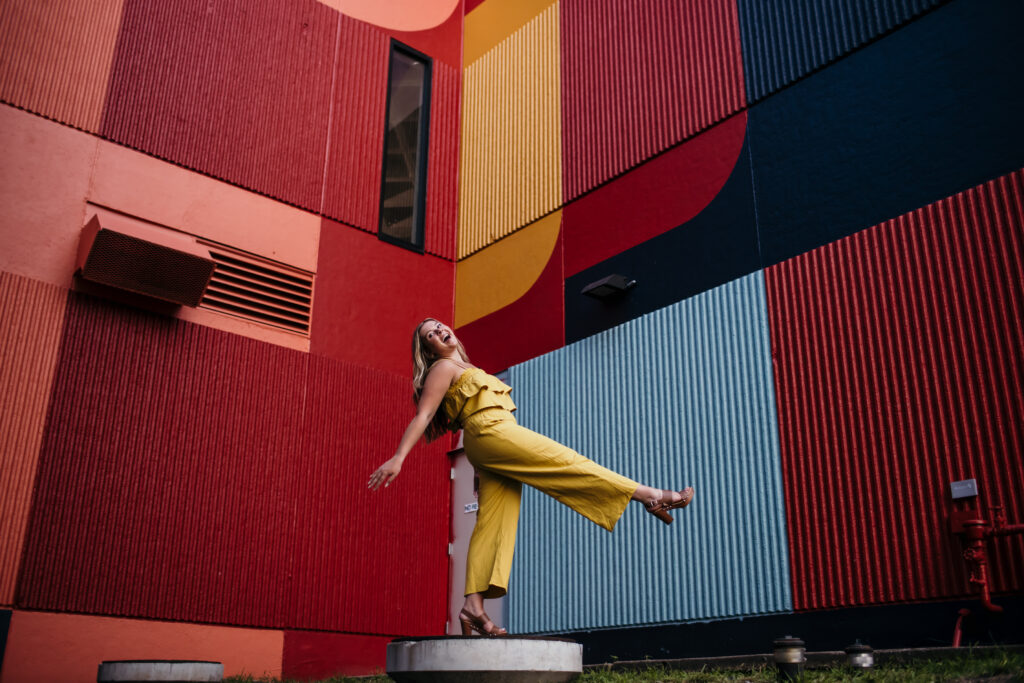 Fun high school senior photo with leg kick in front of mural wall
