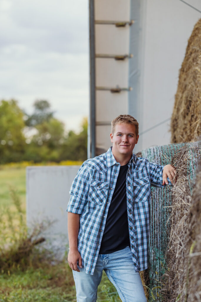 Senior boy photo session in a blue plaid shirt with hay bales