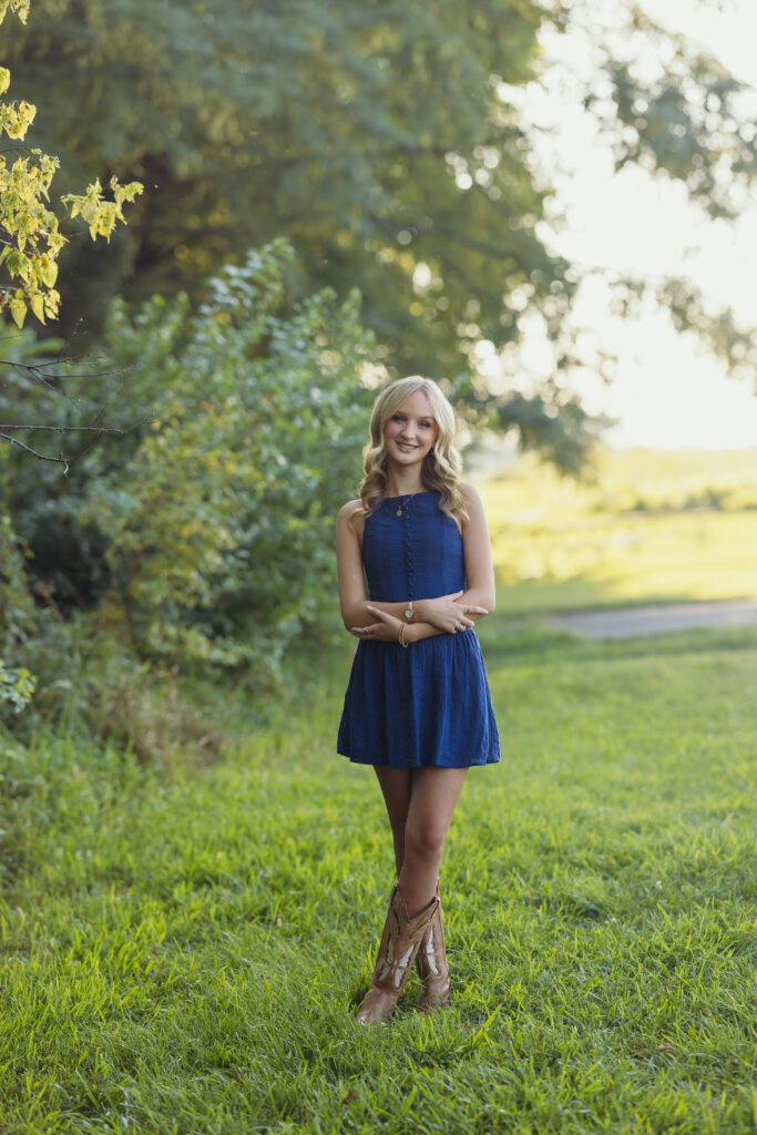 High school senior girl in park setting with navy blue dress and cowboy boots