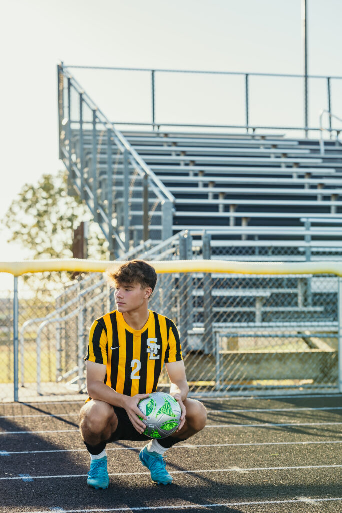 High school senior boy in soccer uniform posing at his high school stadium