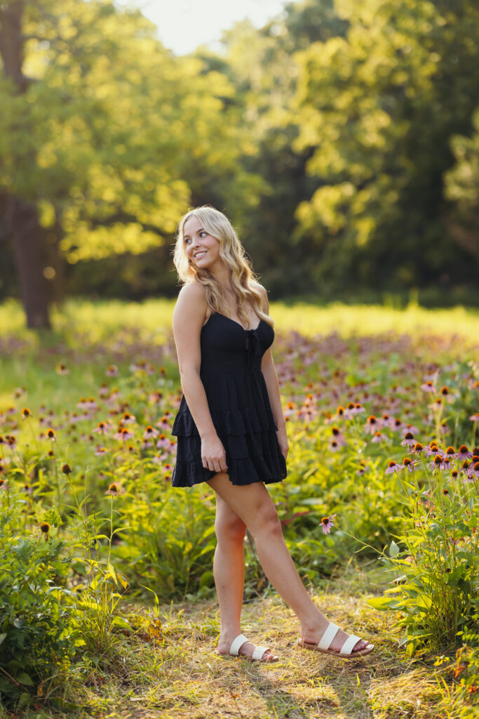 High school senior in black dress standing in a field of wildflowers