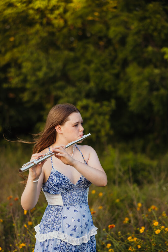 High school senior playing flute during golden hour in a wildflower field