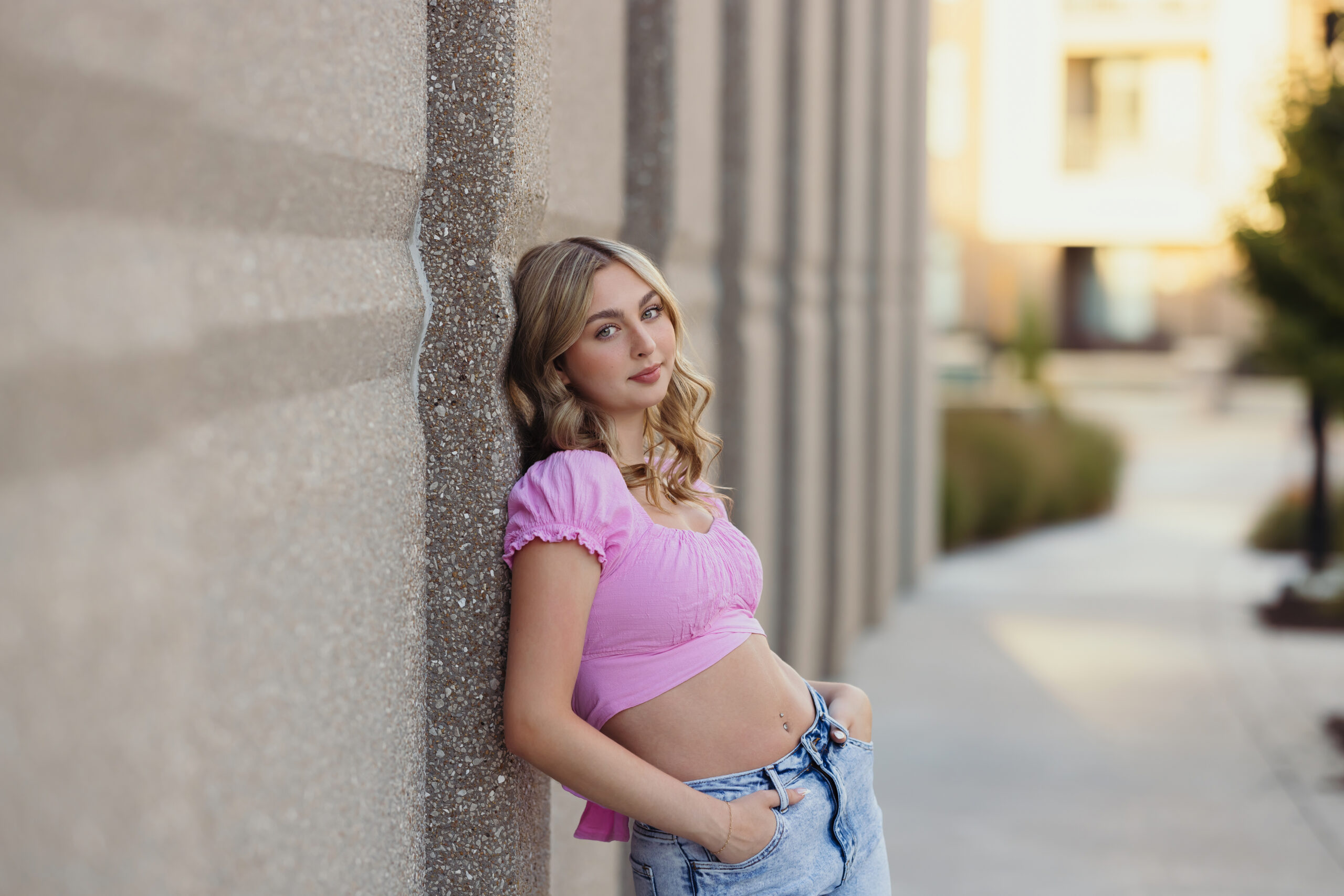 Kansas City high school senior posing in Lenexa, KS with pink shirt and stone walls