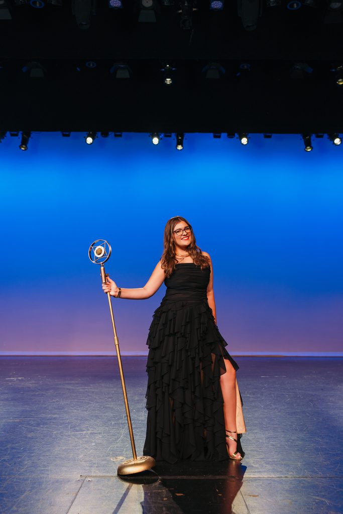 Kansas City senior portrait with a vintage microphone on her high school auditorium stage