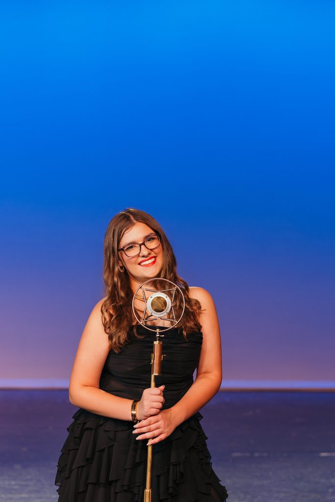 Kansas City senior portrait of Chacey with a vintage microphone on her high school auditorium stage