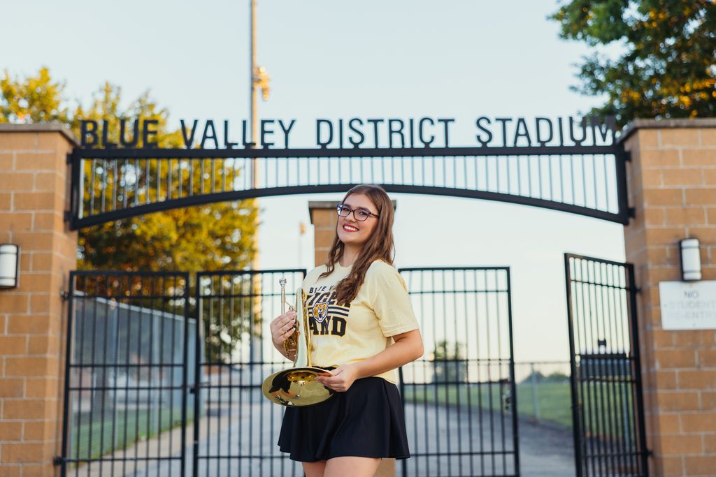 Kansas City senior pictures featuring her trumpet on the football field at sunset