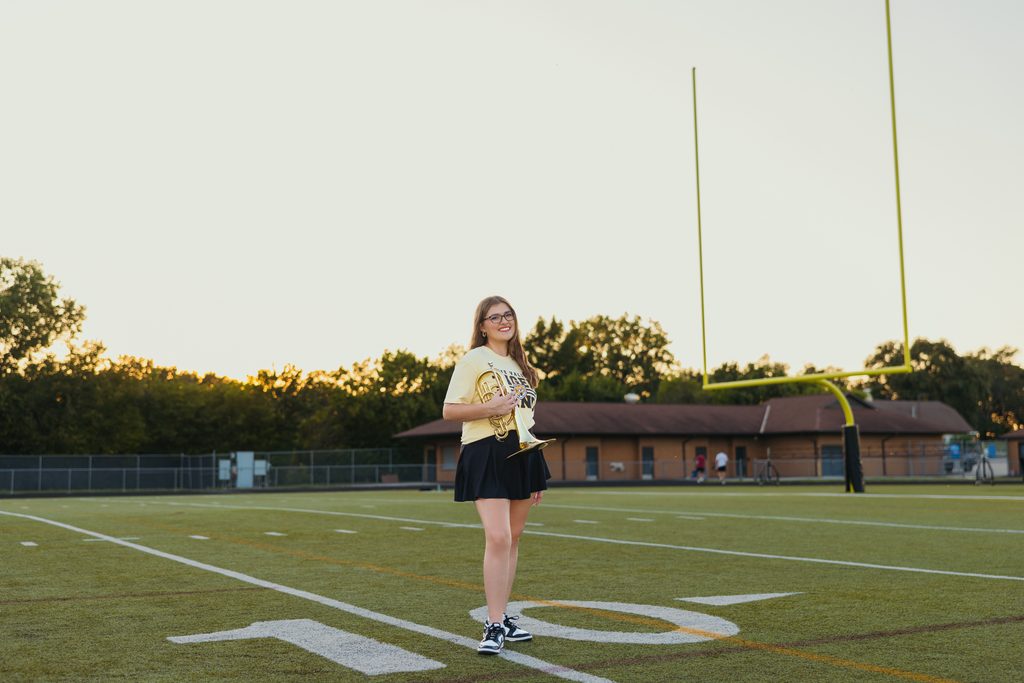 Kansas City senior pictures featuring her trumpet on the football field at sunset