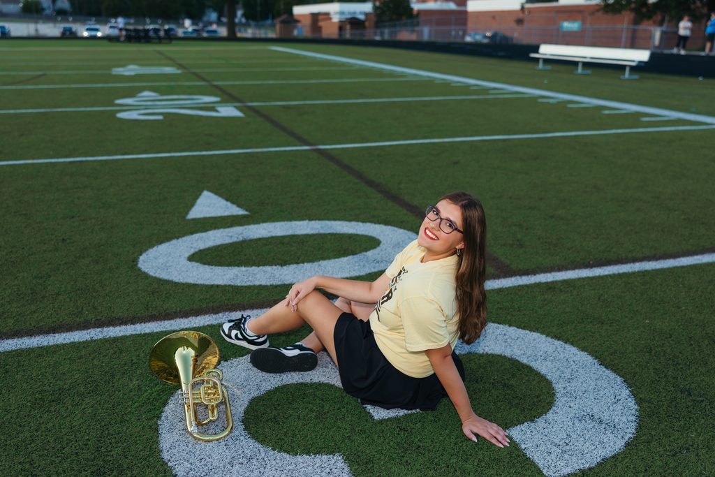 Kansas City senior pictures featuring her trumpet on the football field at sunset