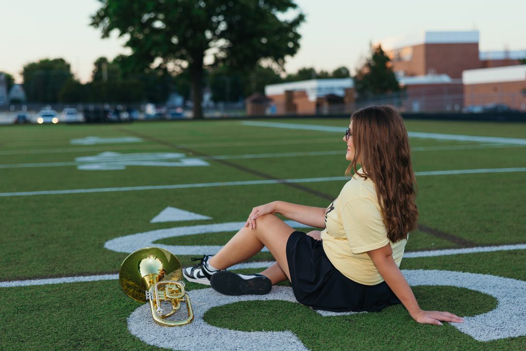 Kansas City senior pictures featuring her trumpet on the football field at sunset