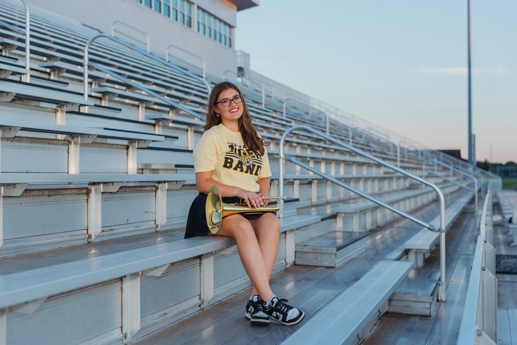 Kansas City senior pictures featuring her trumpet on the football field at sunset