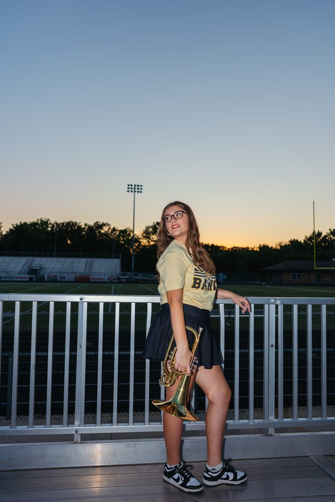Kansas City senior pictures featuring her trumpet on the football field at sunset