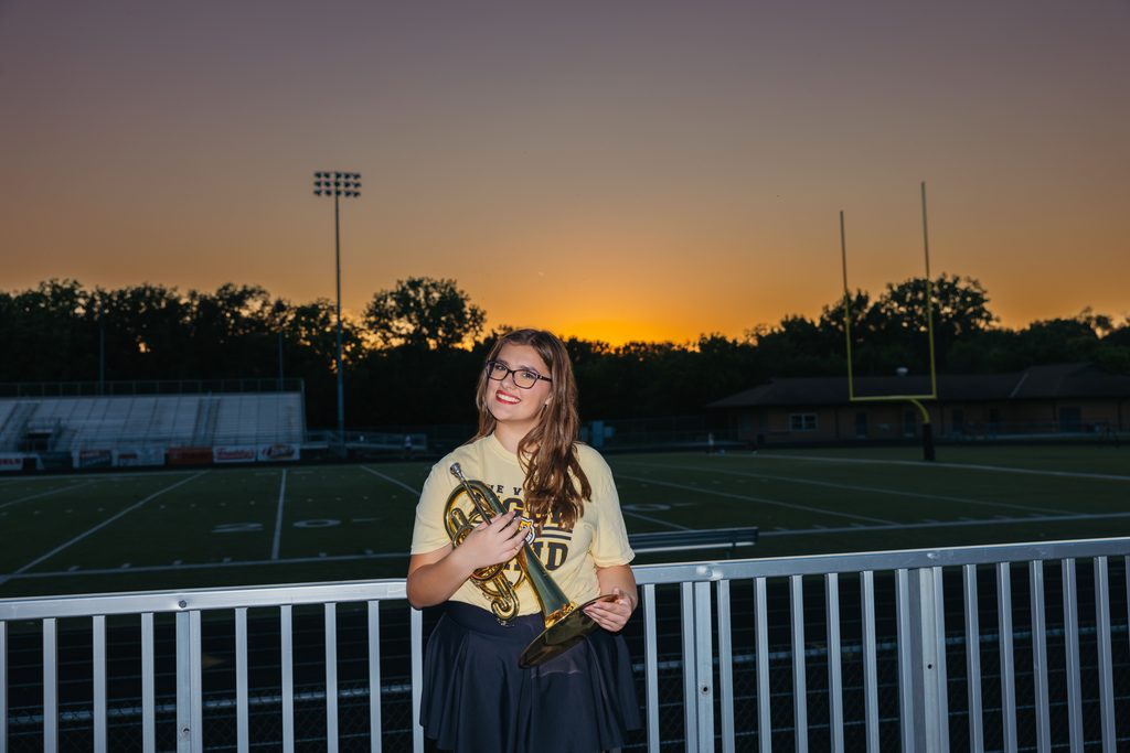Kansas City senior pictures featuring her trumpet on the football field at sunset