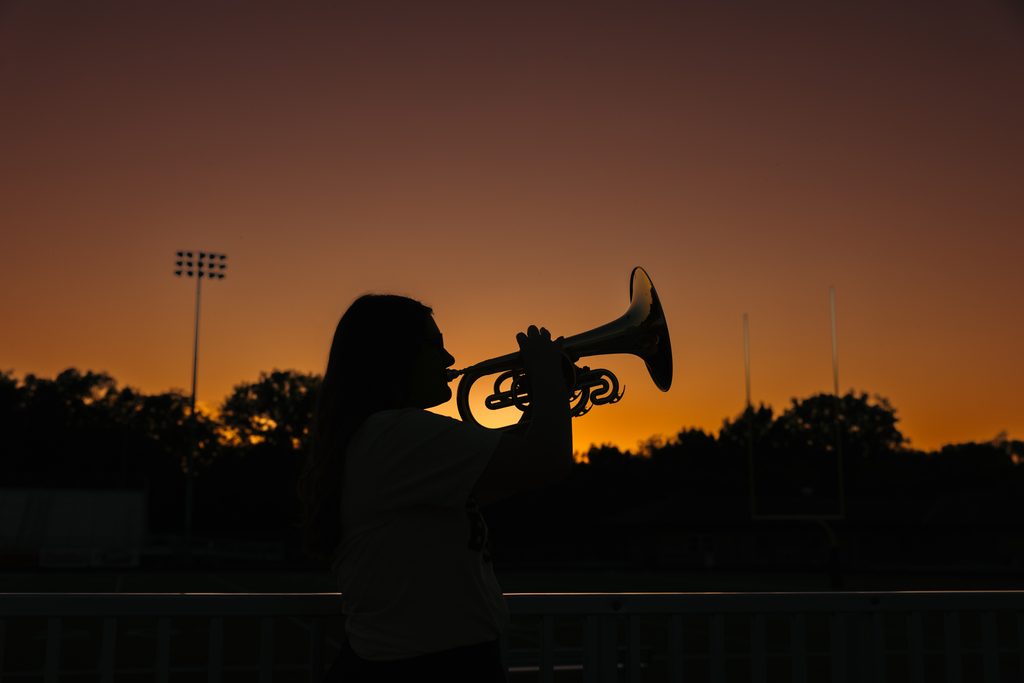 Kansas City senior pictures featuring her trumpet on the football field at sunset